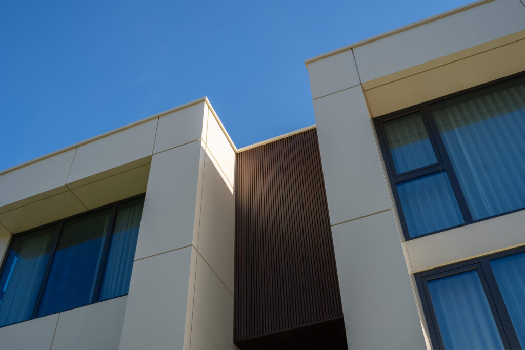 Upper facade detail at 23 Granlea Rd showing ETT Tan Alpolic ACM panels, Rosewood fluted panel transition, and modern window alignment.