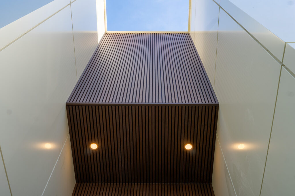 Hidden entrance detail at 23 Granlea Rd with Rosewood fluted composite panel soffit, recessed lighting, and ETT Tan ACM side panels.