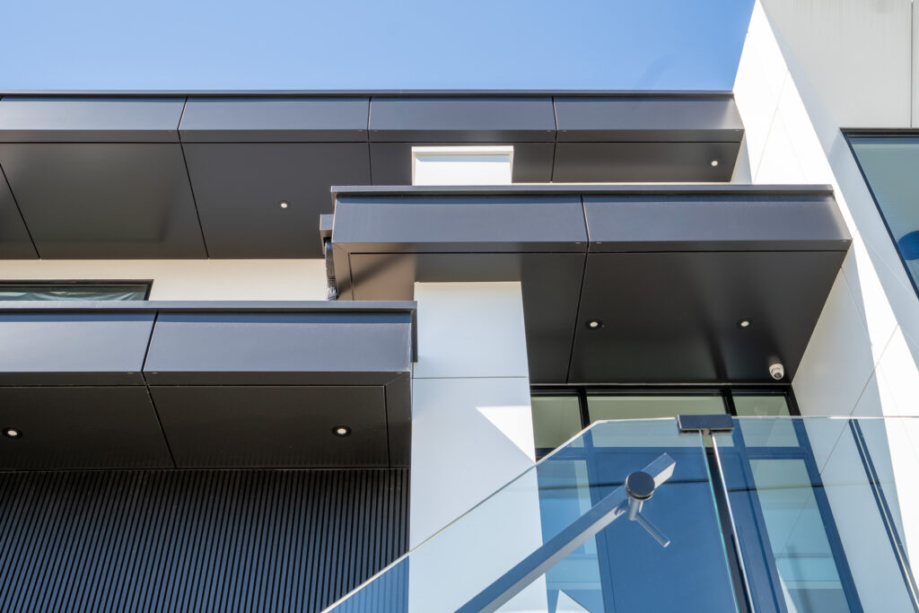 Close-up of ACM soffit and return detailing at 61 Deevale Rd with Midnight Black and Off-White panels, glass railing, and sharp facade edges.