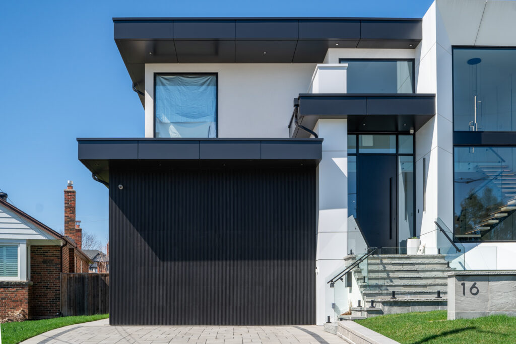 Straight-on view of 61 Deevale Rd showing black ACM garage door cladding aligned with surrounding wall panels for a hidden-door facade effect.