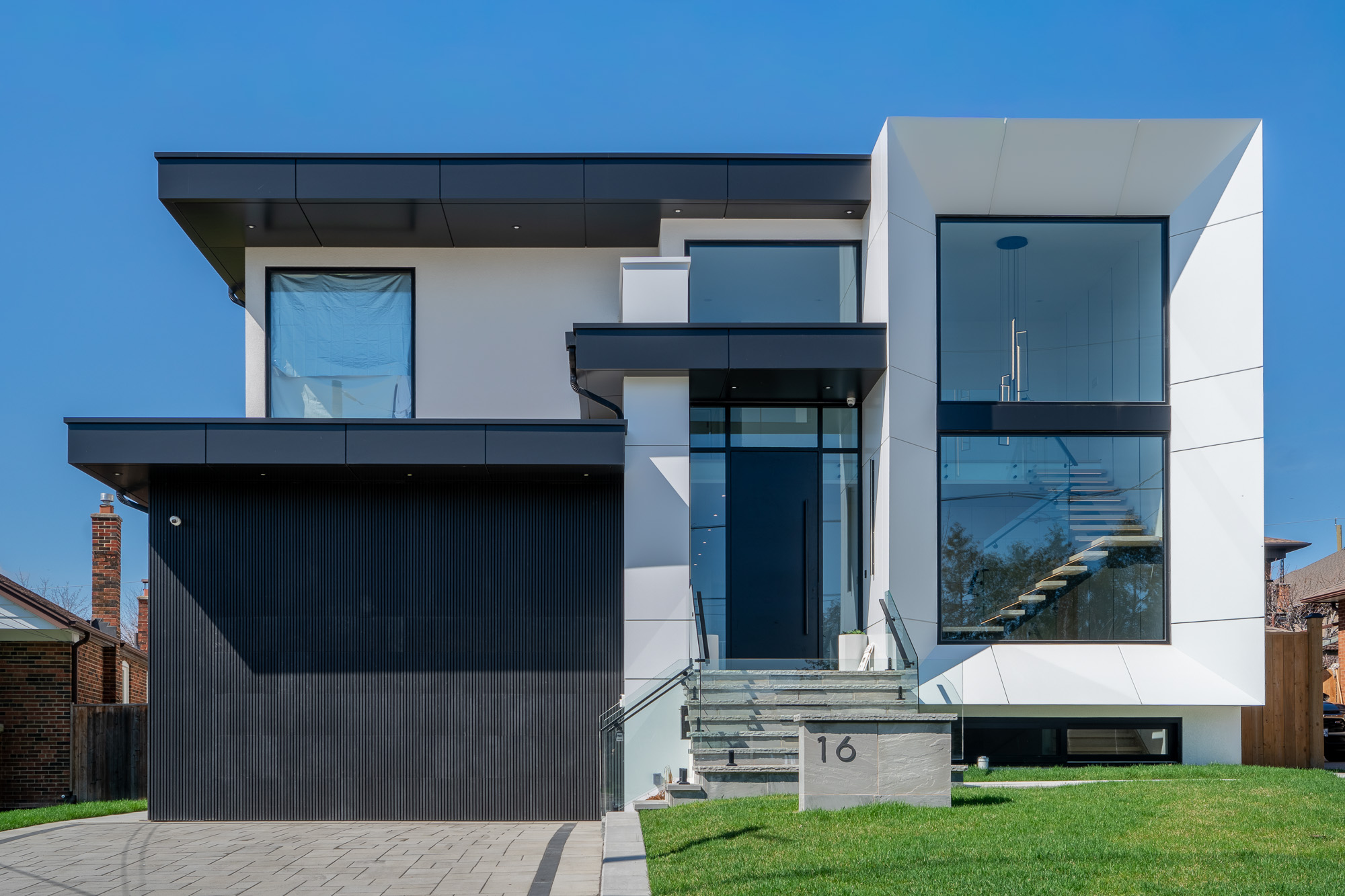 Front view of 61 Deevale Rd with hidden garage door cladding, Midnight Black ACM panels, Off-White ACM returns, and glass entry detailing.