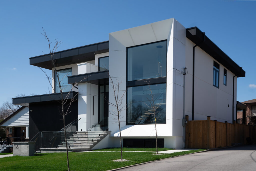 Angled view of 61 Deevale Rd with Off-White Ideabond ACM panel returns, black garage cladding, large glass window, and sharp modern exterior edges.