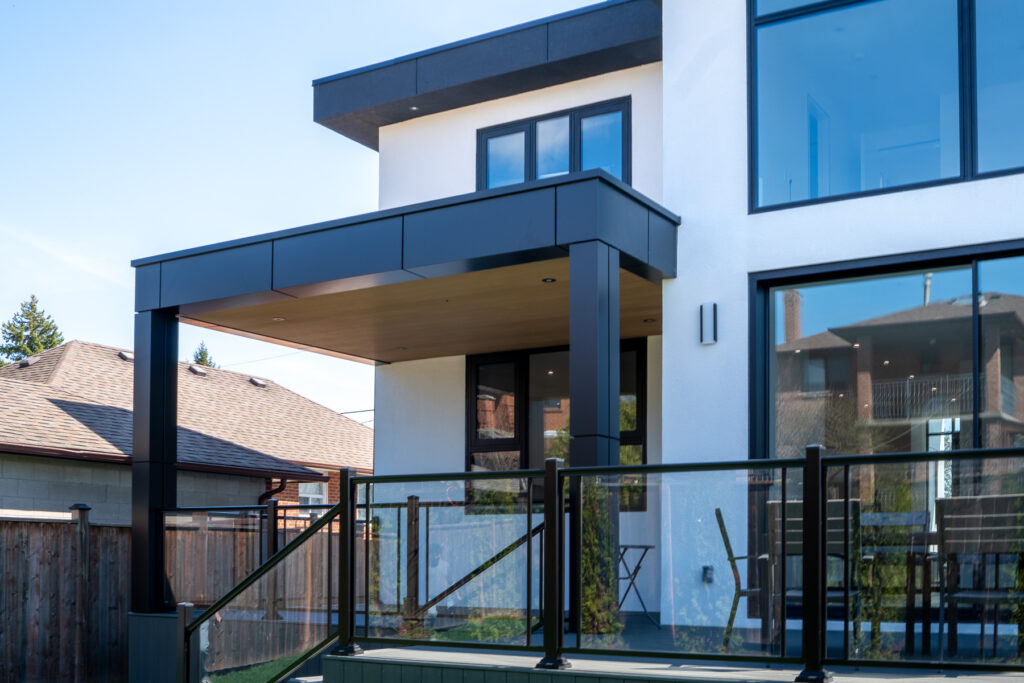Rear facade detail at 61 Deevale Rd with CladMart Creamy Cedar fluted composite panels, black ACM canopy, glass railing, and modern exterior cladding.